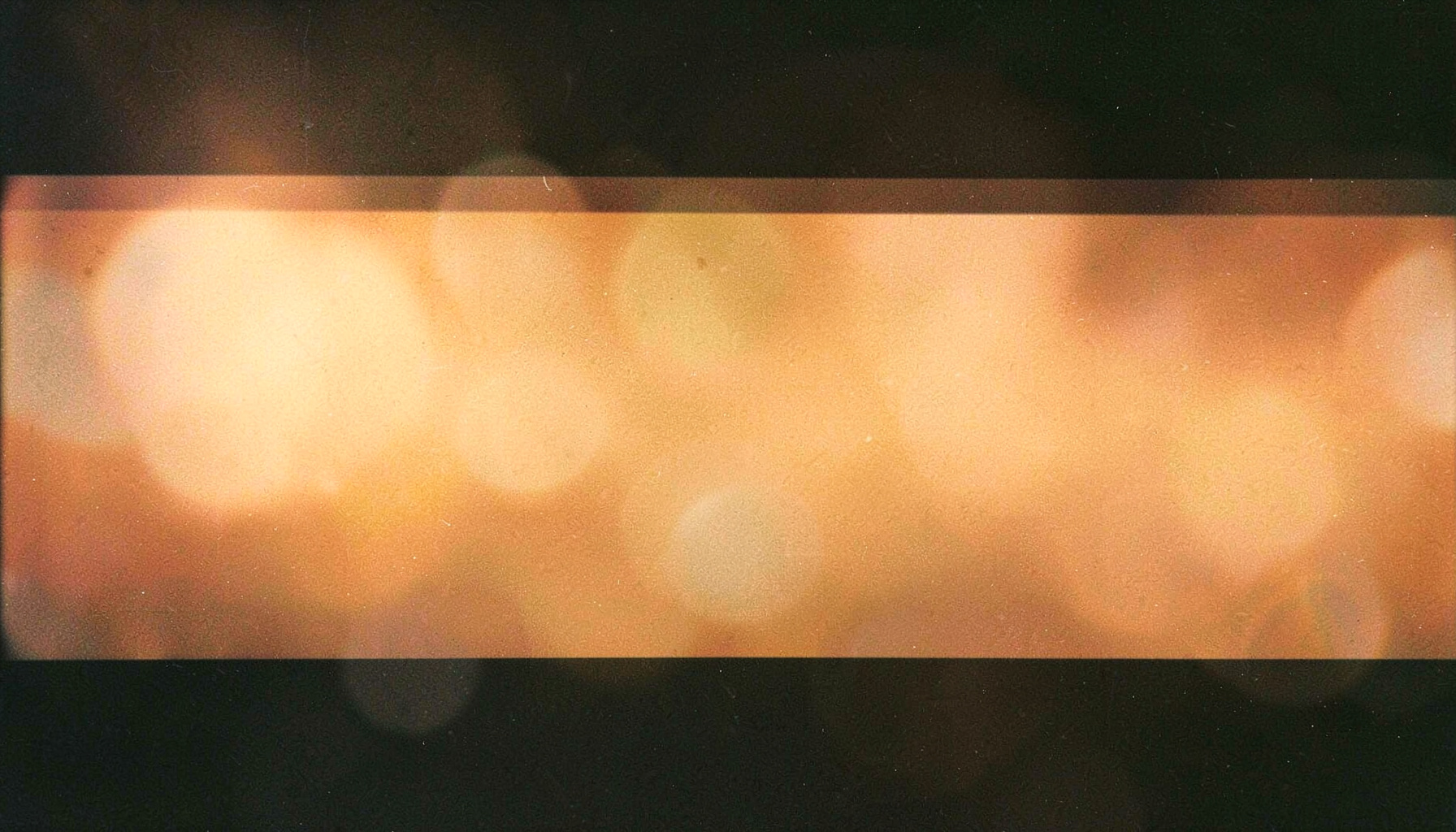 Warm amber gradient banner with soft lens flare bokeh on a dark background, analog film photograph with visible grain
