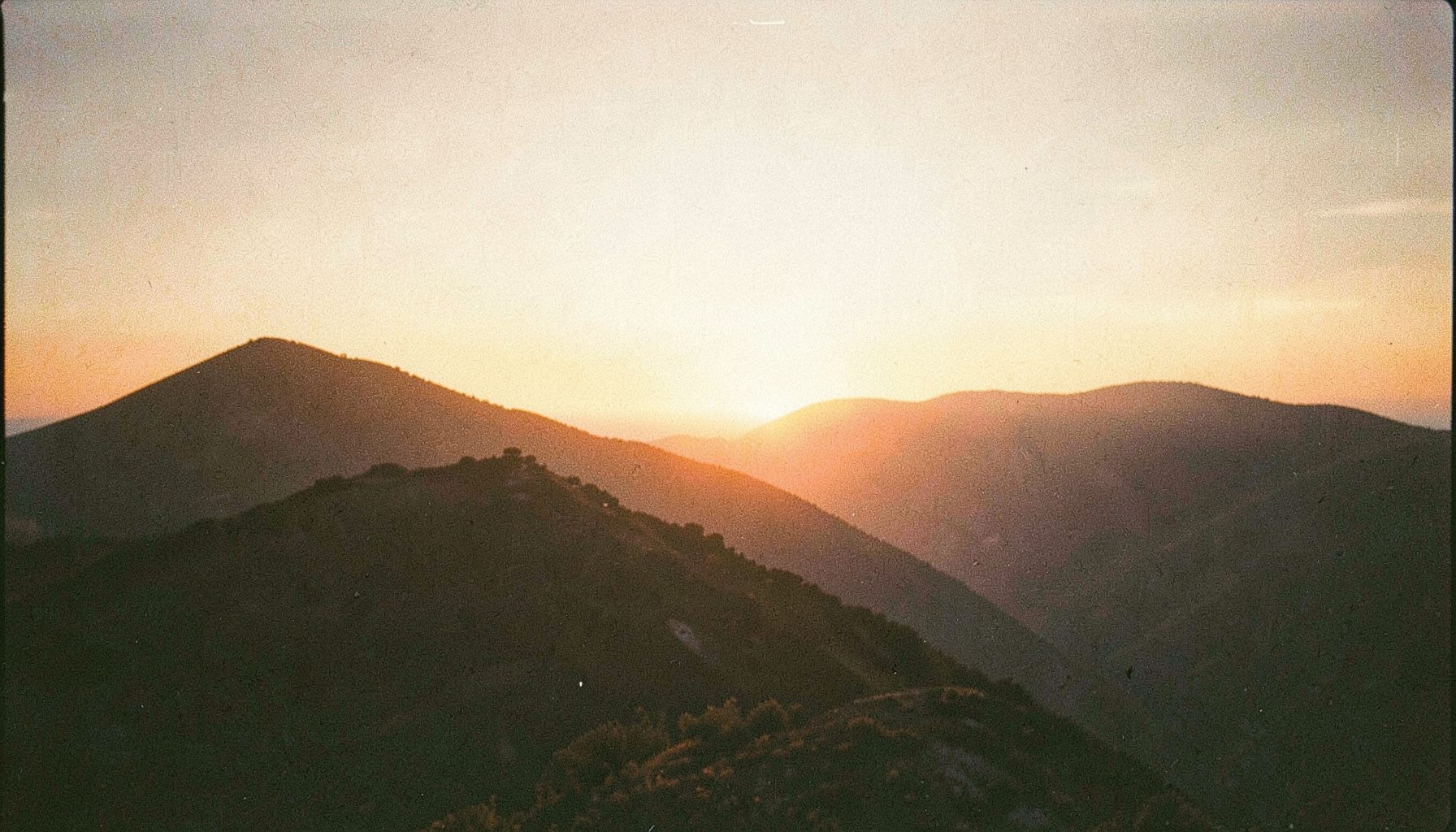 Warm sunset over a ridge, captured on analog film with visible grain and soft golden-to-amber tones evoking a calm, contemplative mood