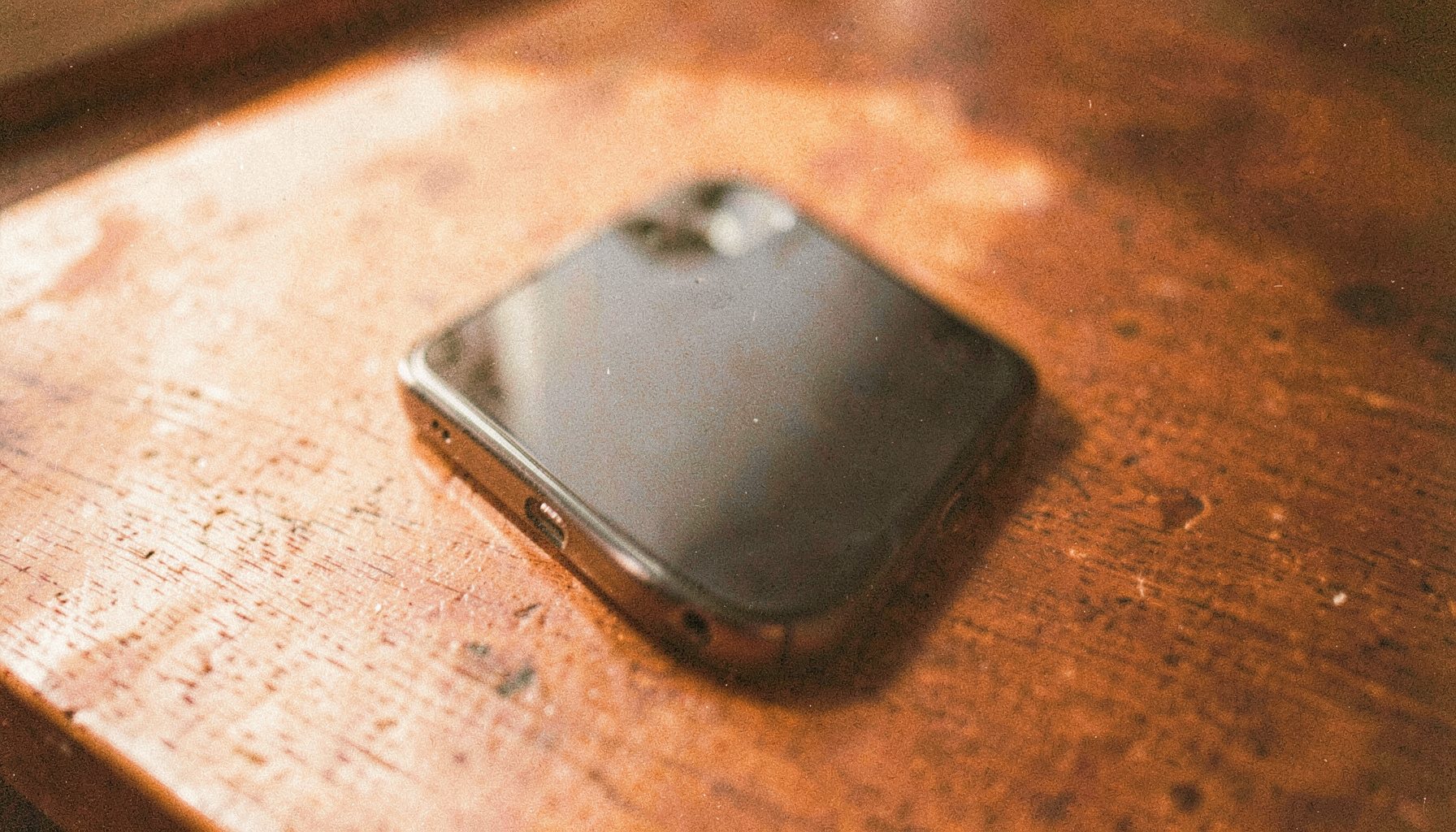 Smartphone on a wooden table with warm natural light, analog film grain, muted amber and rust hues