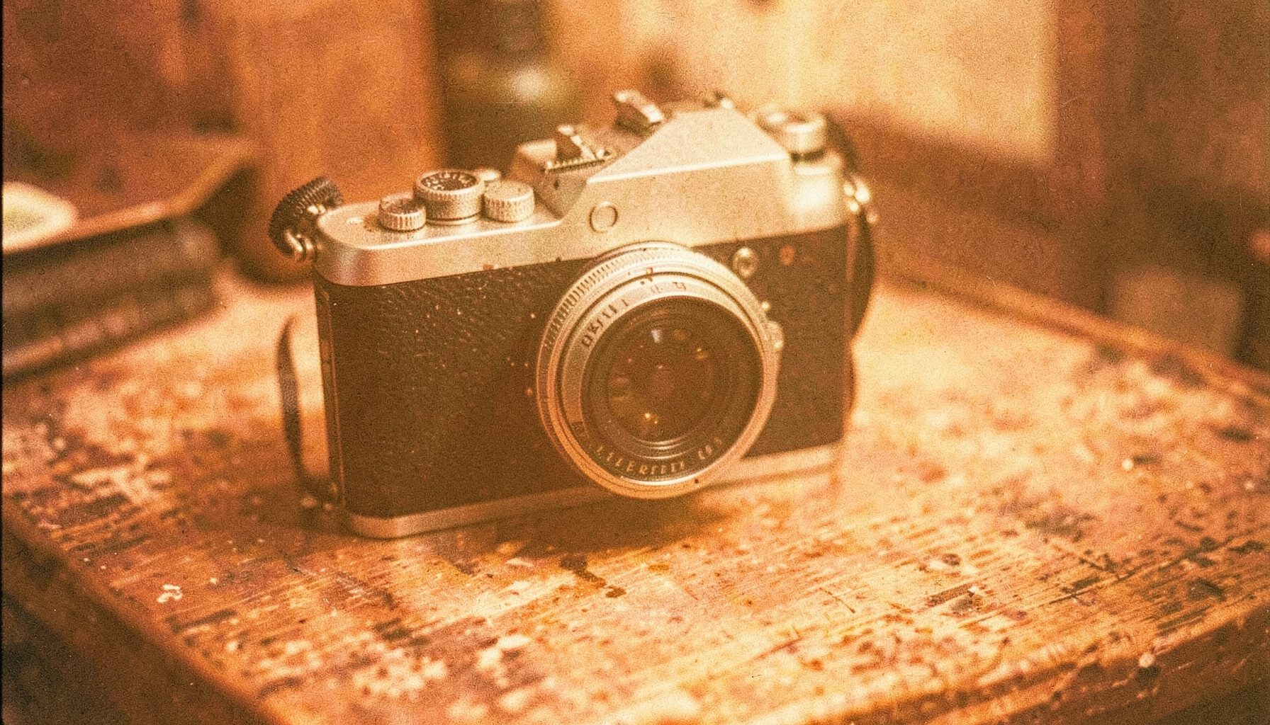 Vintage camera on a weathered wooden desk, warm amber light, grainy analog film photograph