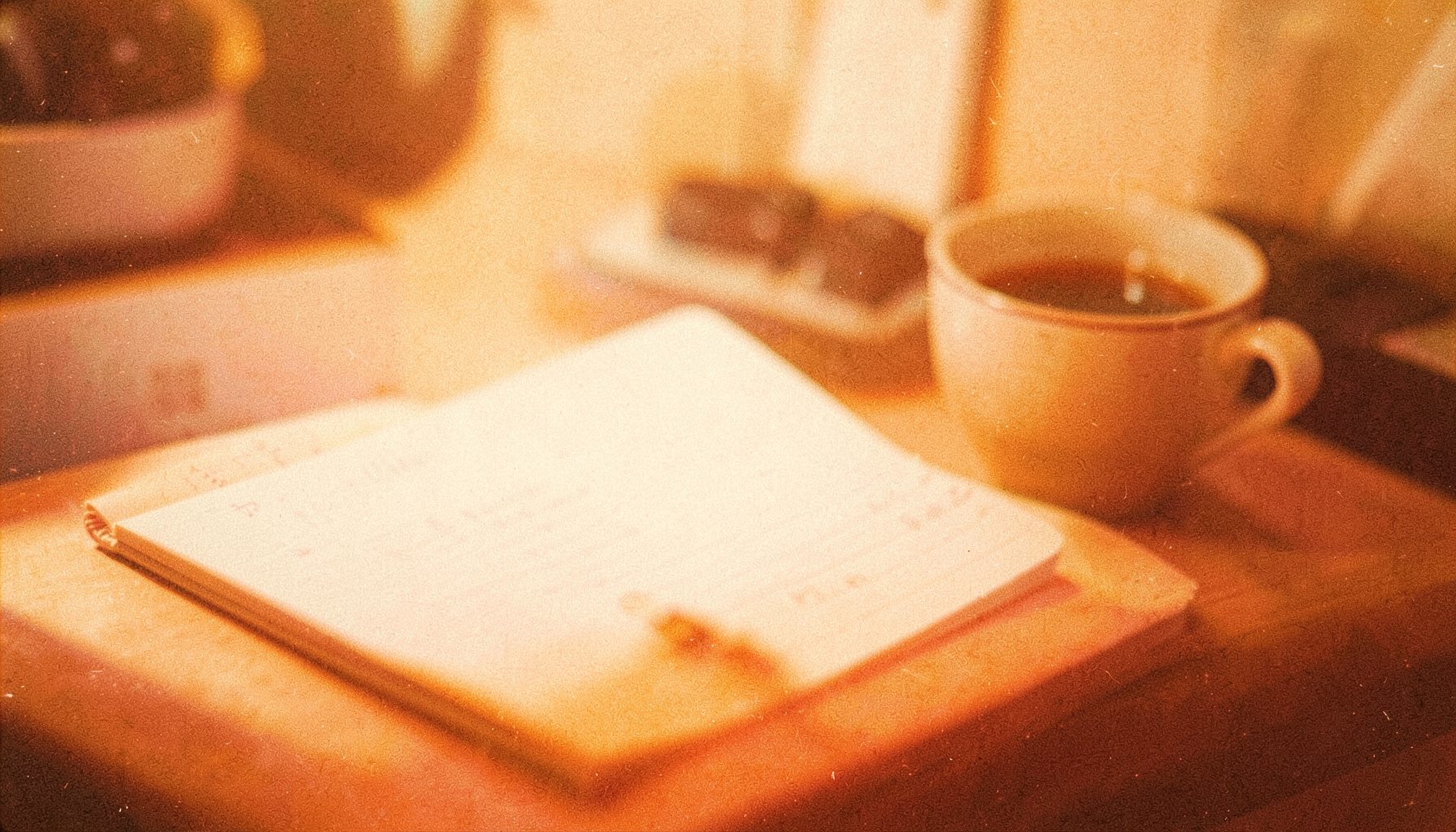 Softly lit desk with a notebook and coffee cup, warm orange and cream tones, grainy analog film look